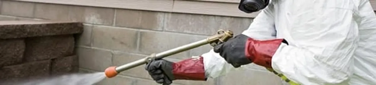 Pest control technician applying exterior insect treatment along a home foundation in Arvada, CO