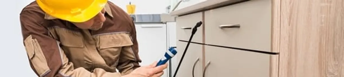 Roach exterminator applying treatment under kitchen cabinets in Arvada, CO