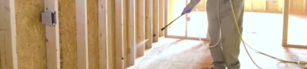 Termite treatment technician applying spray along framing and unfinished walls in Arvada, CO